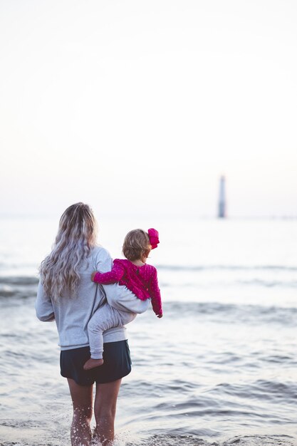 Vertikale Aufnahme einer Mutter, die ihr Baby hält und den Seehorizont betrachtet