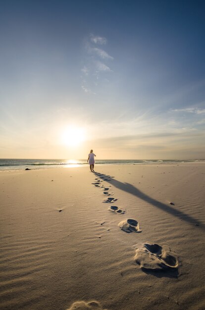 Vertikale Aufnahme einer Person, die am Sandstrand mit Schritten im Vordergrund spaziert