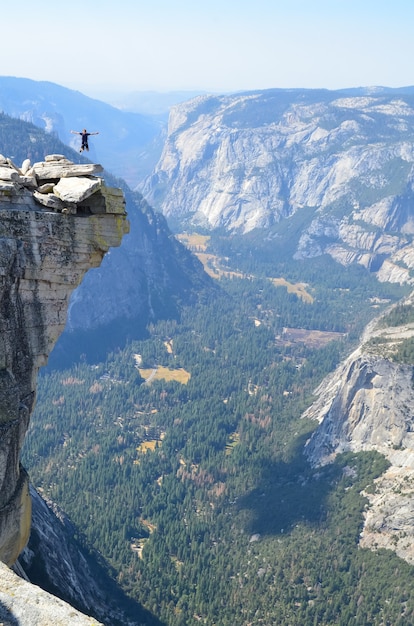Vertikale Aufnahme einer Person, die auf eine Klippe bei Half Dome, Yosemite, Kalifornien springt