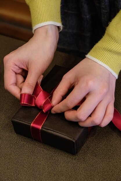 Vertikale Aufnahme einer Person, die ein Geschenk mit einem niedlichen roten Band einwickelt