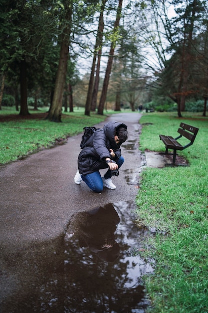 Kostenloses Foto vertikale aufnahme einer person, die eine aufnahme der wasserpfütze in einem park macht