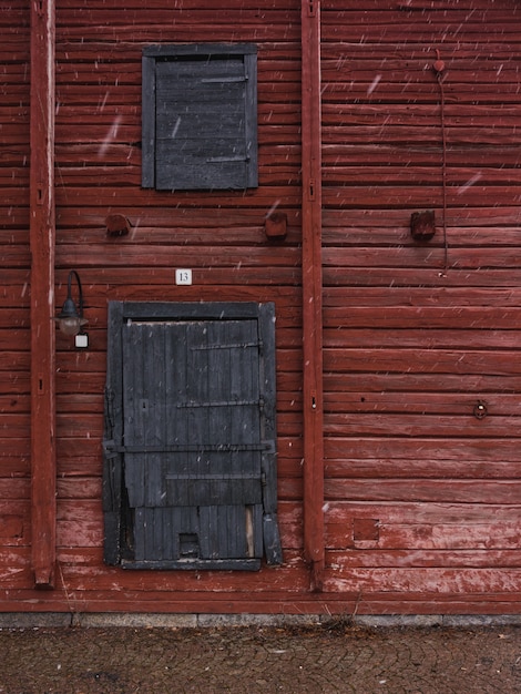 Vertikale Aufnahme einer roten Holzwand mit grauen Holztüren im Winter