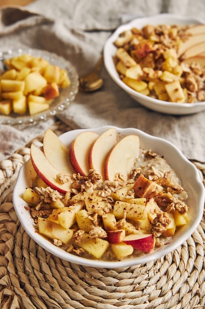 Vertikale Aufnahme einer Schüssel Brei mit Müsli und Nüssen und Apfelscheiben auf einem Tisch