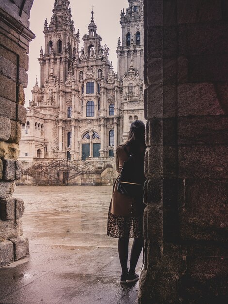 Vertikale Aufnahme einer stilvollen Frau in der Kathedrale von Santiago de Compostela in Spanien an einem regnerischen Tag