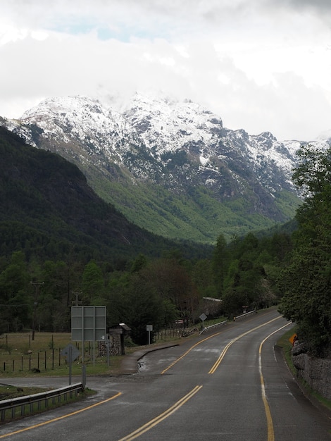 Vertikale Aufnahme einer Straße und baumbedeckter Berge mit schneebedeckten Gipfeln