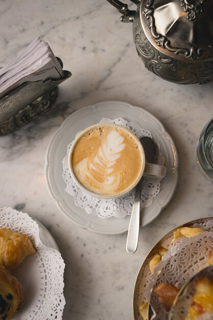 Vertikale Aufnahme einer Tasse Cappuccino auf dem Marmortisch mit Desserts