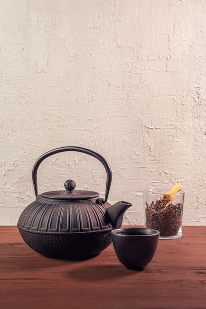 Vertikale Aufnahme einer Teekanne aus japanischem Gusseisen, einer Teetasse aus Keramik und eines losen schwarzen Tees in einem Glas