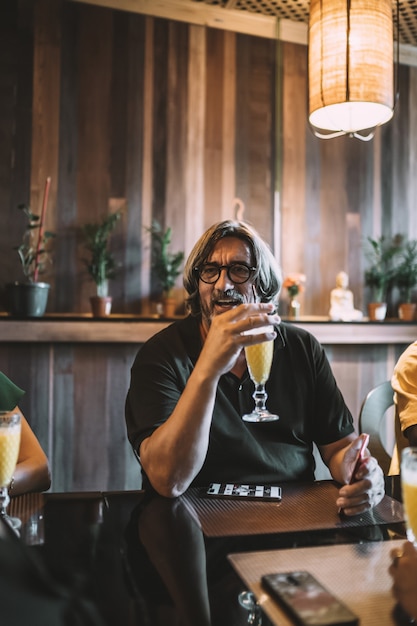 Vertikale Aufnahme eines älteren Mannes mit langen Haaren, der in einem Restaurant einen Smoothie trinkt?