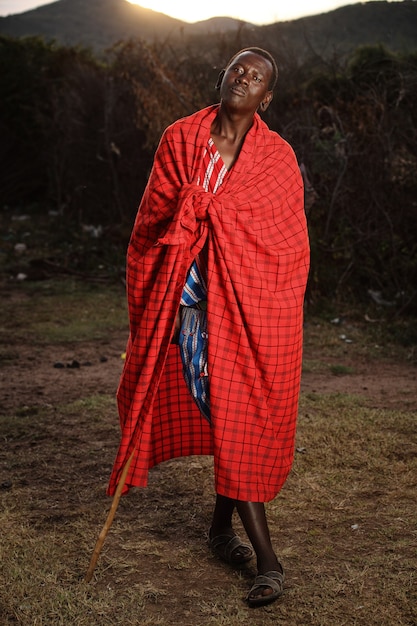 Kostenloses Foto vertikale aufnahme eines afrikanischen mannes mit einer decke um ihn herum, während er einen stock hält