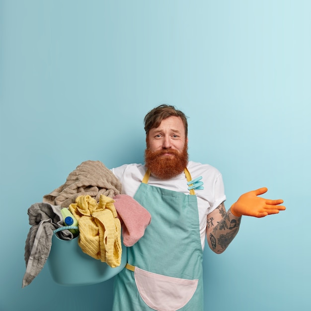 Kostenloses Foto vertikale aufnahme eines ahnungslosen ahnungslosen rothaarigen mannes kann kein waschmittel zum waschen von wäsche wählen