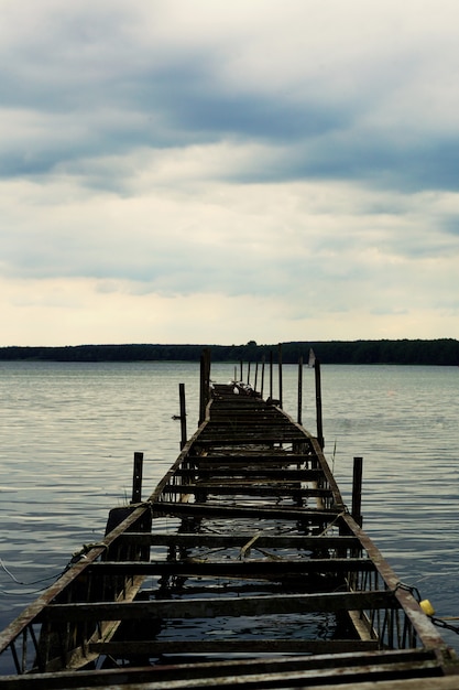 Kostenloses Foto vertikale aufnahme eines alten halb gebrochenen piers mit bewölktem himmel in miedwie, stargard, polen.