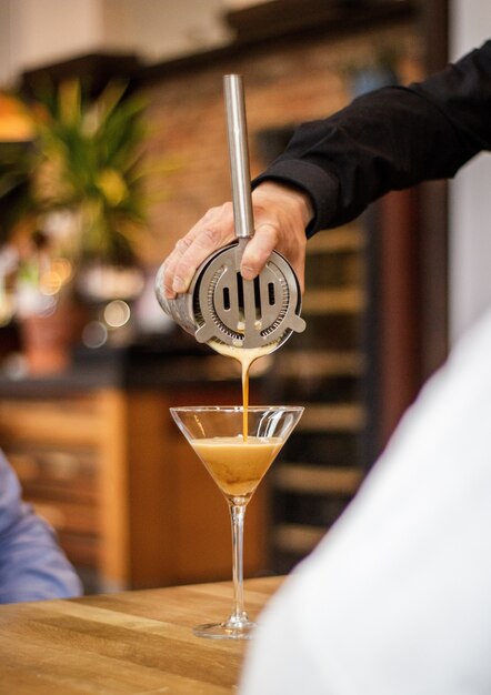 Vertikale Aufnahme eines Barkeepers, der den Cocktail in ein Glas mit einem unscharfen Hintergrund gießt