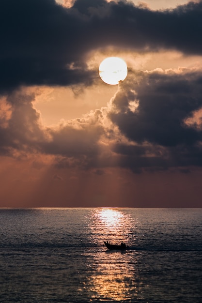 Vertikale Aufnahme eines Bootes in einem Meer bei Sonnenuntergang