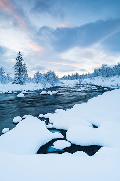 Vertikale Aufnahme eines Flusses mit Schnee darin und eines Waldes nahe bedeckt mit Schnee im Winter in Schweden