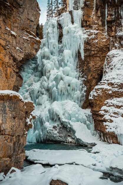 Vertikale Aufnahme eines gefrorenen Wasserfalls, umgeben von Felsformationen