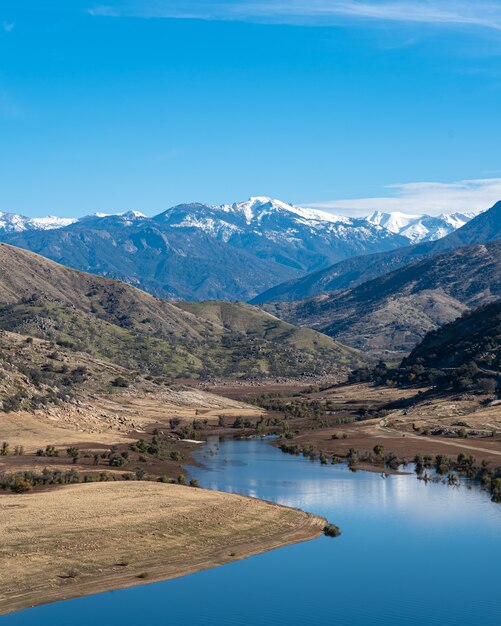 Vertikale Aufnahme eines gewundenen Flusses mit majestätischen Bergen und blauem Himmel