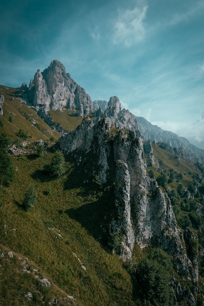 Vertikale Aufnahme eines grasbewachsenen Hügels mit Bäumen nahe felsigen Klippen und blauem Himmel