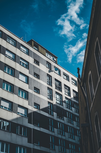 Vertikale Aufnahme eines grauen und weißen Gebäudes mit Fenstern unter einem blauen Himmel