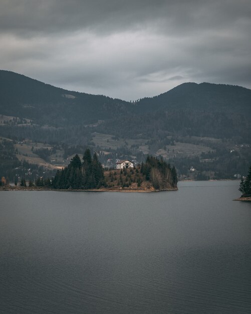 Vertikale Aufnahme eines Hauses an der Küste, umgeben von Bäumen und Bergen