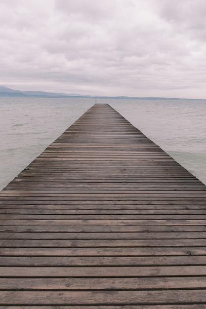 Kostenloses Foto vertikale aufnahme eines hölzernen piers über dem ruhigen ozean unter dem schönen bewölkten himmel