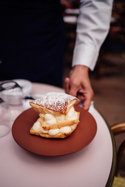 Vertikale Aufnahme eines Kellners, der einen köstlichen Millefeuille-Kuchen mit Puderzucker serviert