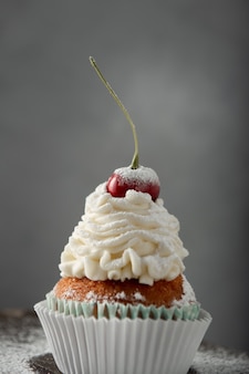 Vertikale aufnahme eines köstlichen cupcakes mit sahne, puderzucker und einer kirsche an der spitze