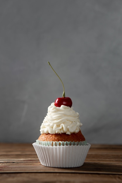 Vertikale Aufnahme eines köstlichen Cupcakes mit Sahne und Kirsche an der Spitze