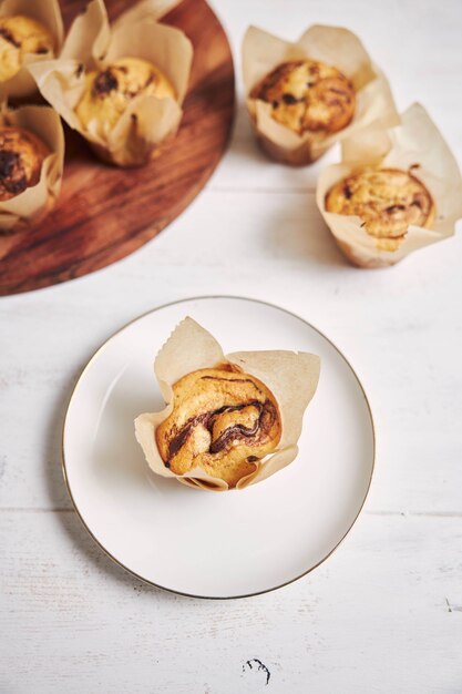 Vertikale Aufnahme eines köstlichen Schokoladenmuffins in der Nähe einer Holzplatte auf einem weißen Teller