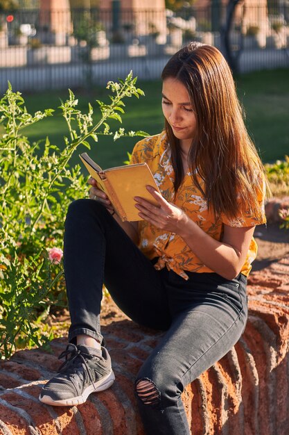Vertikale Aufnahme eines Mädchens in einem gelben Hemd, das ein Buch liest, das neben Pflanzen sitzt