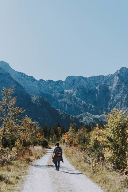 Kostenloses Foto vertikale aufnahme eines männlichen wanderers, der sich durch eine schmale schotterstraße in richtung felsiger berge wagt