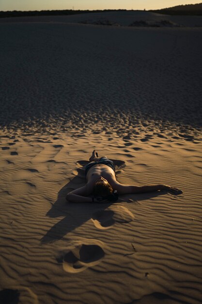 Vertikale Aufnahme eines Mannes, der auf dem Sand in einer verlassenen Landschaft bei Sonnenuntergang liegt