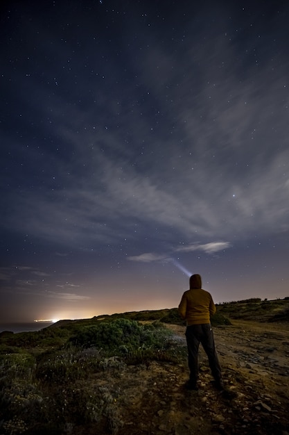 Vertikale Aufnahme eines Mannes, der auf den Felsen steht und die leuchtenden Sterne in der Nacht betrachtet