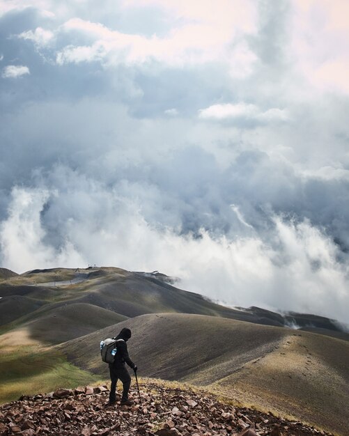 Vertikale Aufnahme eines Mannes, der auf einem Berg mit einem bewölkten Himmel im Hintergrund steht