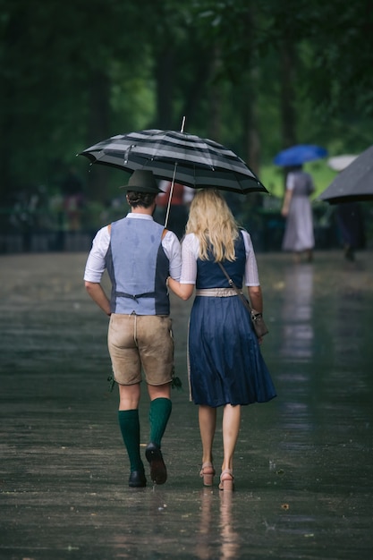 Vertikale aufnahme eines mannes und einer frau, die unter einem regenschirm nebeneinander gehen