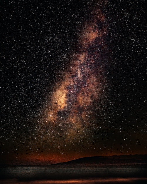 Vertikale Aufnahme eines Meeres unter einem Sternenhimmel mit Milchstraße