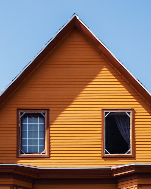 Vertikale Aufnahme eines orangefarbenen Holzhauses unter dem klaren blauen Himmel