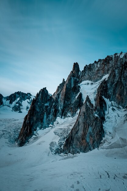 Vertikale Aufnahme eines schneebedeckten Hügels nahe Berg unter einem blauen Himmel