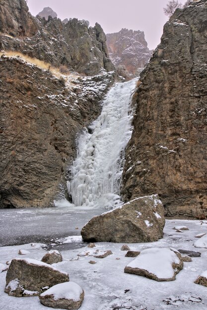 Vertikale Aufnahme eines schönen gefrorenen Wasserfalls zwischen den felsigen Klippen