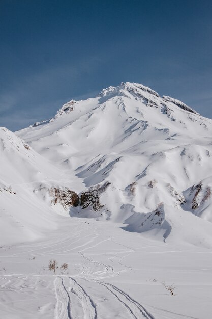 Vertikale Aufnahme eines schönen schneebedeckten Berges, der von einem steilen Hügel mit blauem Himmel im Hintergrund geschossen wird