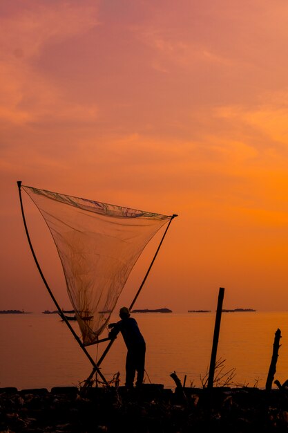 Vertikale Aufnahme eines schönen Sonnenuntergangs über einem Meer mit einem Fischer, der ein Netz hält