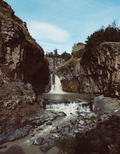 Vertikale Aufnahme eines starken Wasserfalls, der im Fluss zwischen riesigen Felsen fließt