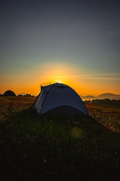 Vertikale Aufnahme eines Zeltes auf einem grünen Hügel bei einem wunderschönen Sonnenaufgang am Morgen