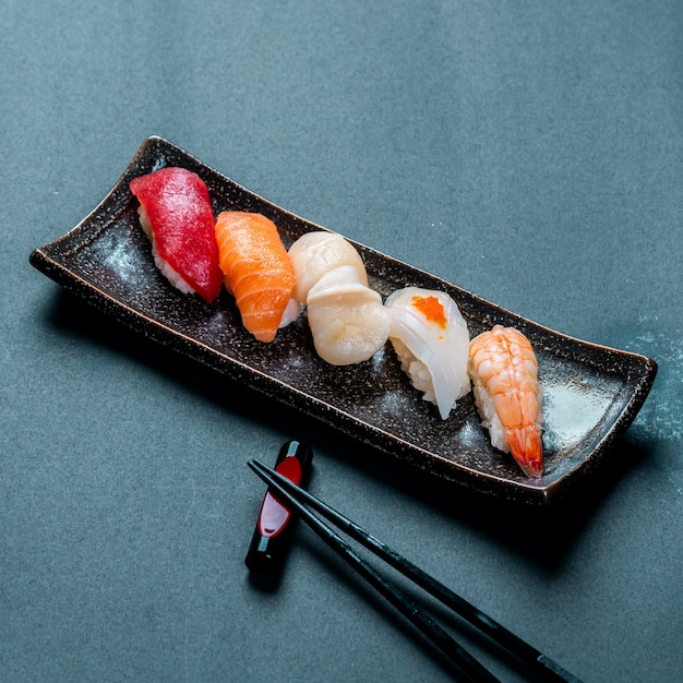 Vertikale aufnahme von frischem thunfisch, lachs, jakobsmuschel, nigiri und shrimps sushi und stäbchen
