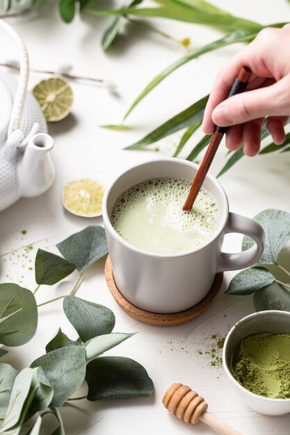 Vertikale Aufnahme von grünem Tee Latte mit Milch in einer weißen Tasse mit grünen Blättern und Holzlöffel