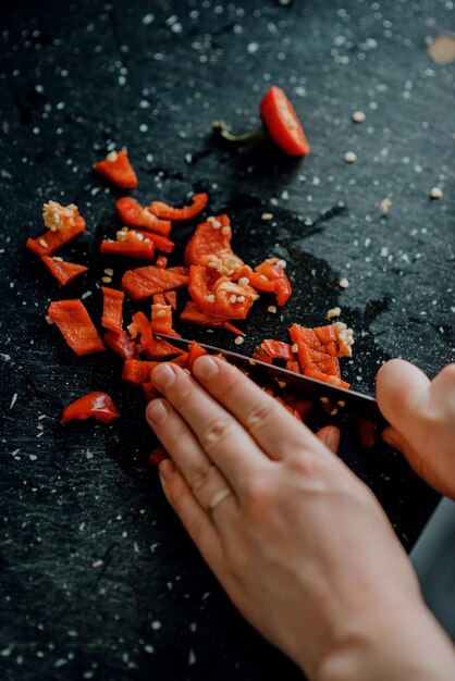 Vertikale Aufnahme von Händen, die eine rote Chilischote auf der schwarzen Oberfläche schneiden