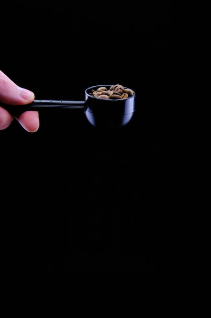 Vertikale Aufnahme von Kaffeebohnen in einer Kaffeeschaufel lokalisiert auf einem schwarzen Hintergrund