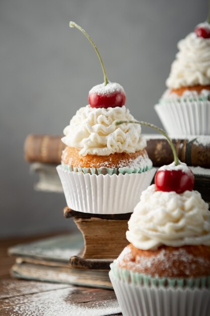 Vertikale Aufnahme von köstlichen Cupcakes mit Sahne, Puderzucker und einer Kirsche oben auf Büchern