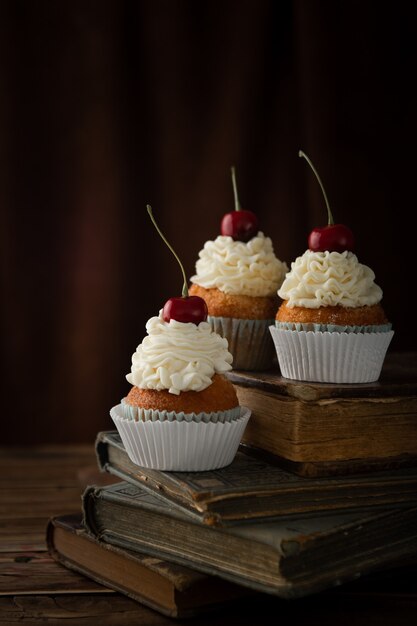 Vertikale Aufnahme von köstlichen Cupcakes mit Sahne und Kirschen oben auf Vintage-Büchern