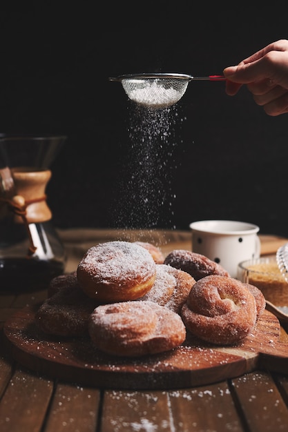 Vertikale Aufnahme von köstlichen Schlangenkrapfen, bestreut mit Puderzucker und Chemex-Kaffee