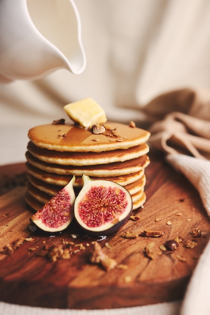 Vertikale Aufnahme von Pfannkuchen mit Sirup, Butter, Feigen und gerösteten Nüssen auf einem Holzteller